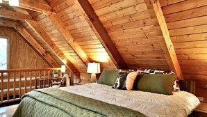 Un dormitorio acogedor en el ático con techo de madera, una cama con ropa de cama verde y blanca, y una mesita de noche con lámpara.