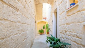 A narrow stone corridor with potted plants and a small shelf with items. - Via Cota 24 (Lecce)