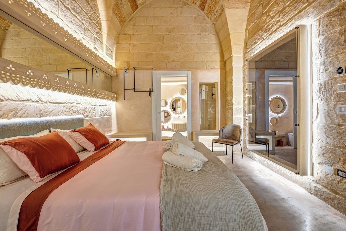 A bedroom with a large bed, a chair, and a mirror.