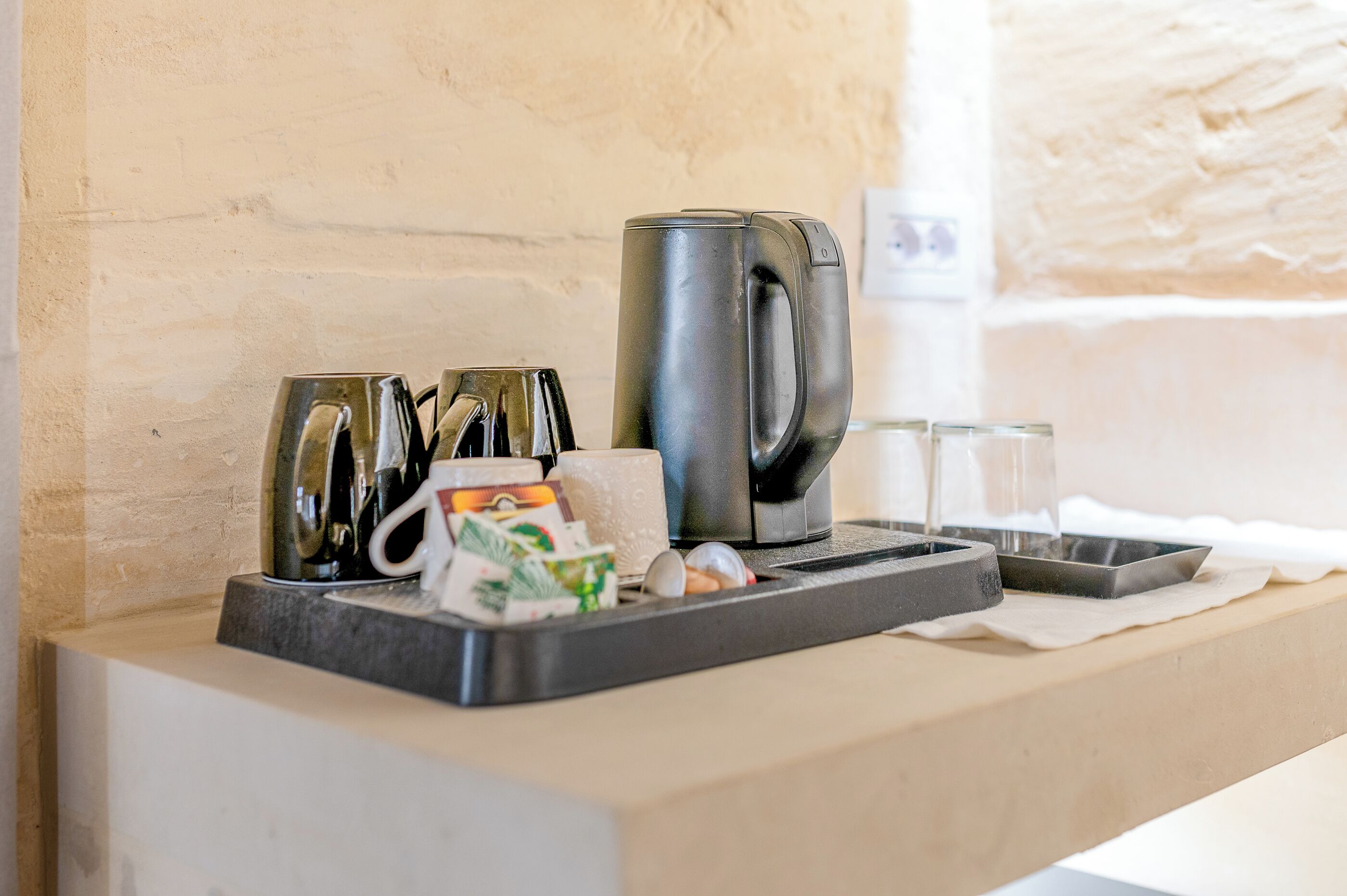A coffee station with a coffee maker, cups, and a tray.