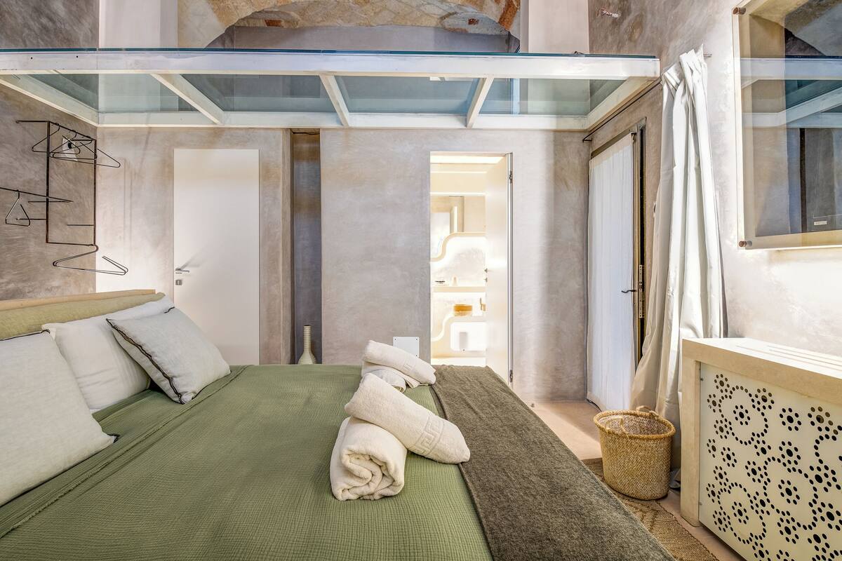 A modern hotel room with a glass ceiling, a neatly made bed, and a visible bathroom in the background.