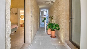 A narrow hallway with stone walls, a bed on the left, and potted plants on the right. - Via Cota 24 (Lecce)