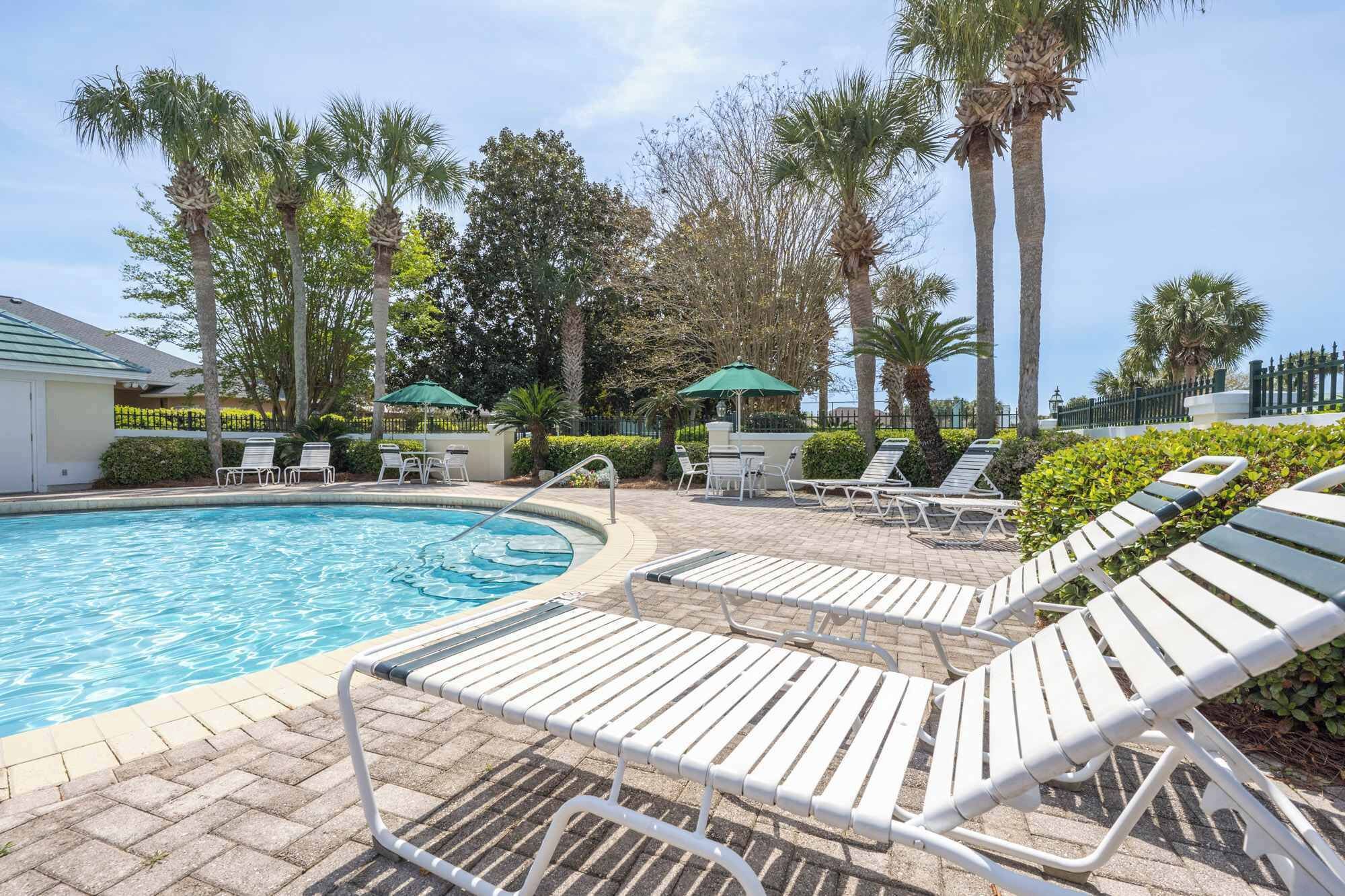 A pool area with lounge chairs, palm trees, and a clear sky.