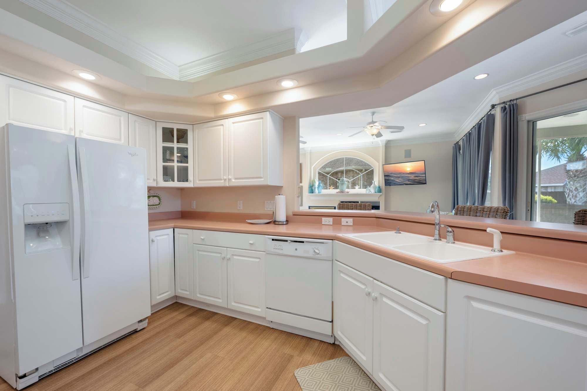 A modern kitchen with white cabinetry, a built-in dishwasher, and a large window with a view of the outdoors.