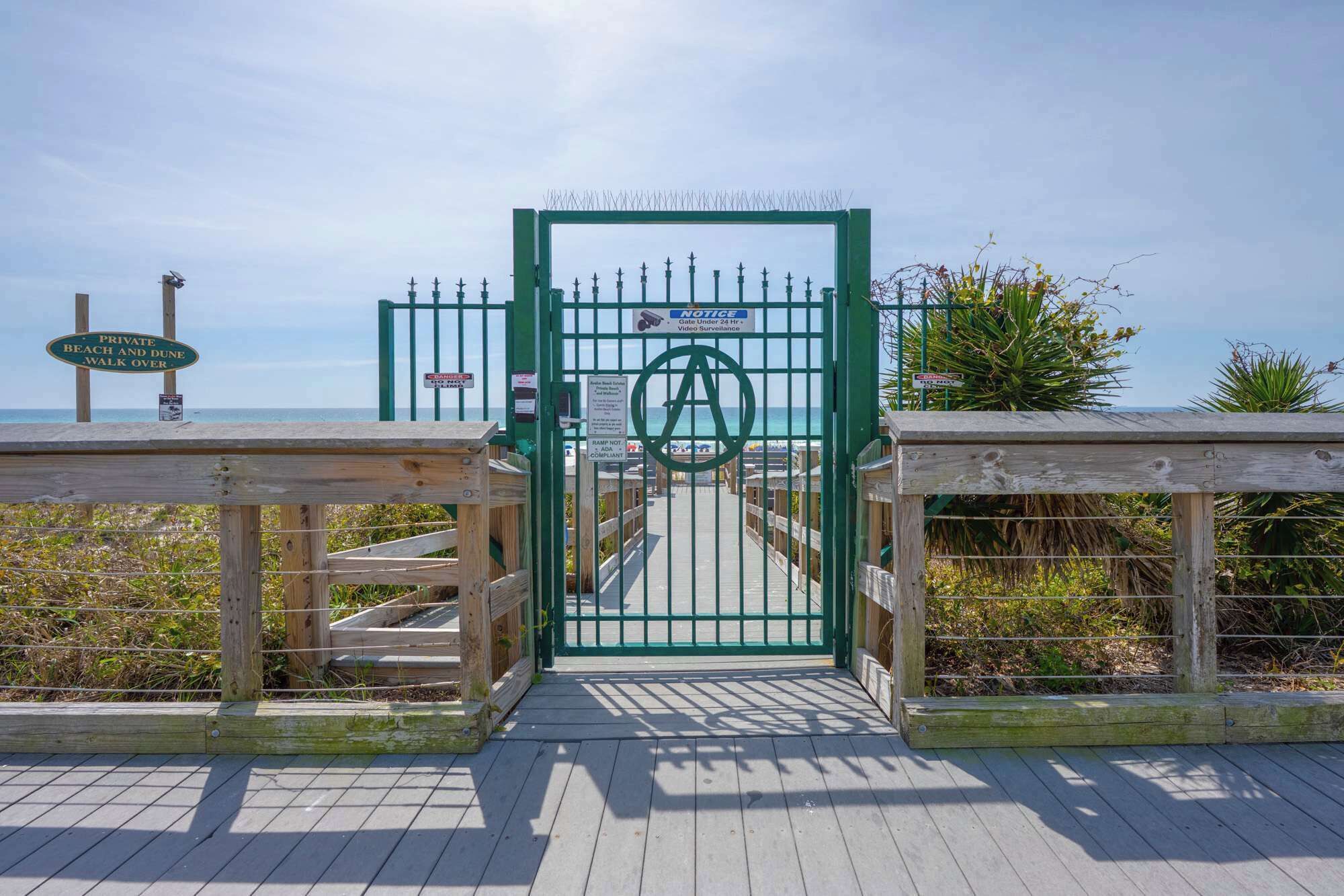 A gated entrance to a private beach and dune walkover area with a wooden walkway leading to the gate.