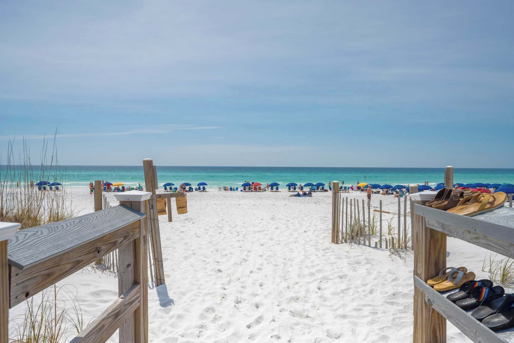 A beach with wooden walkways leading to the sand, and a row of beach shoes on the right.