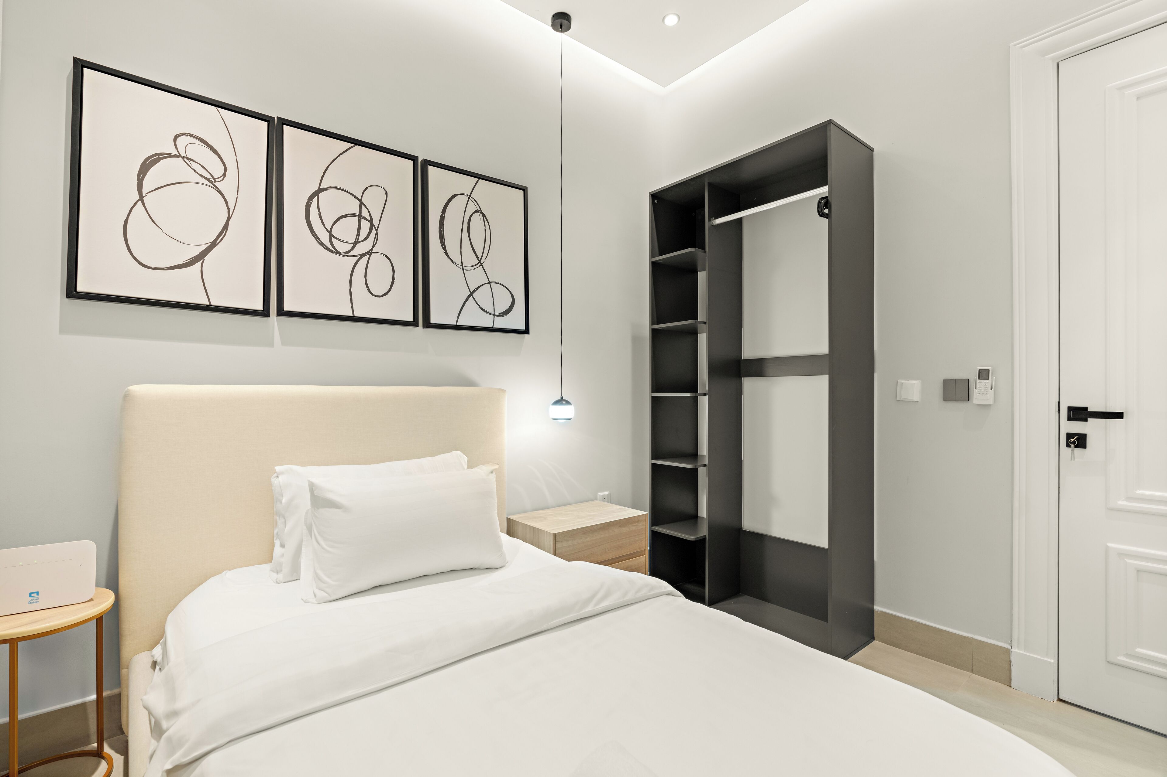 Een moderne slaapkamer met een groot bed, een nachtkastje, een kledingkast en abstracte wanddecoratie.