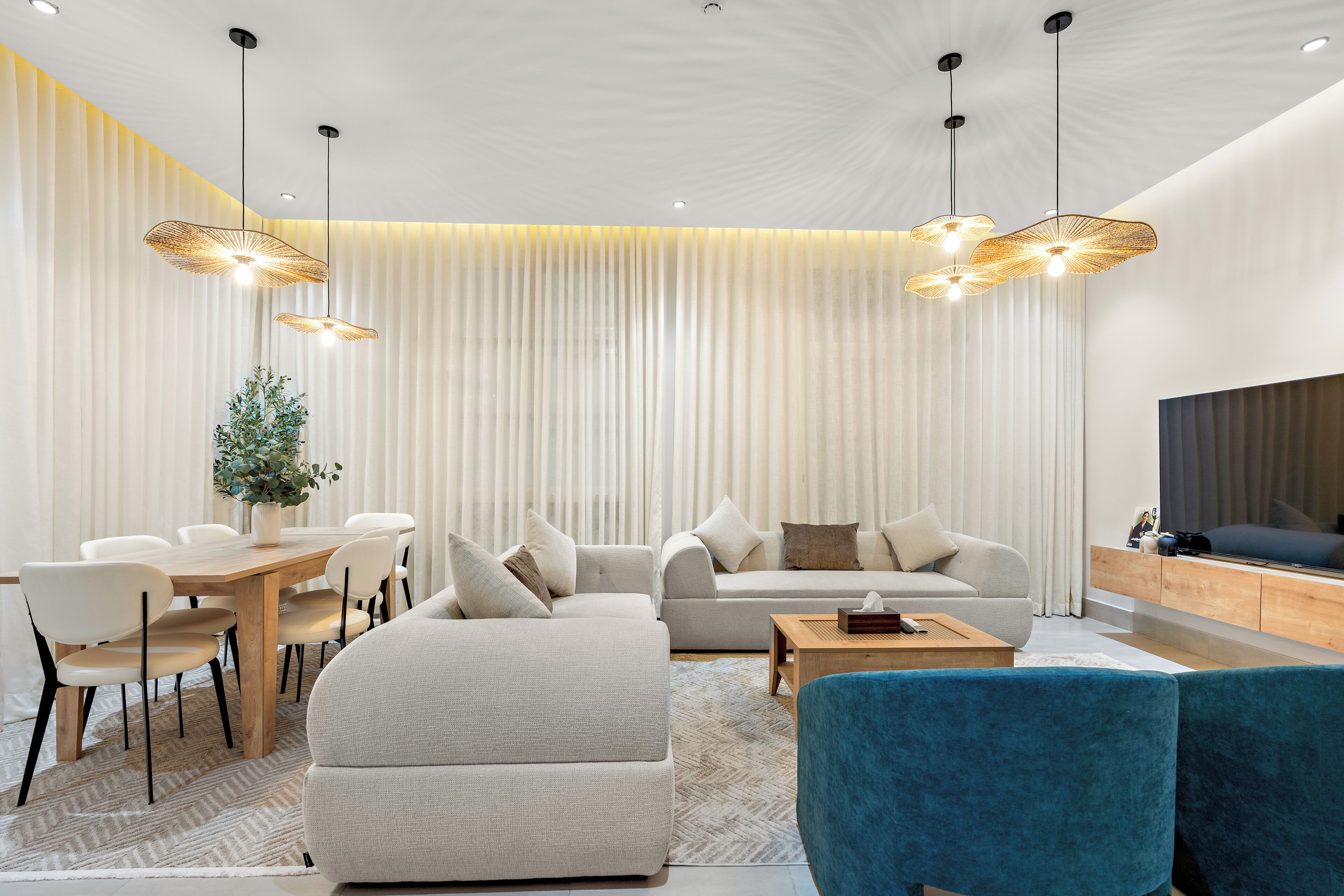 A modern living room with a dining area, featuring a sofa, chairs, a coffee table, and pendant lighting.