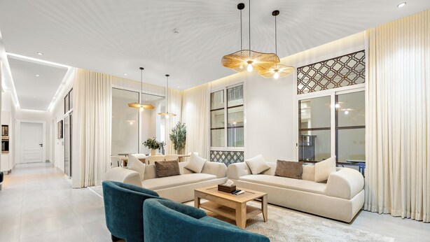 A modern living room with a sectional sofa, two blue armchairs, a coffee table, and pendant lighting. - Silkhaus Majidia 120 (Riyadh)