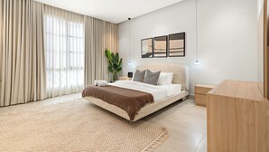 A modern bedroom with a large bed, a wooden nightstand, a bedside table, and a large window with curtains. - Silkhaus Majidia 120 (Riyadh)