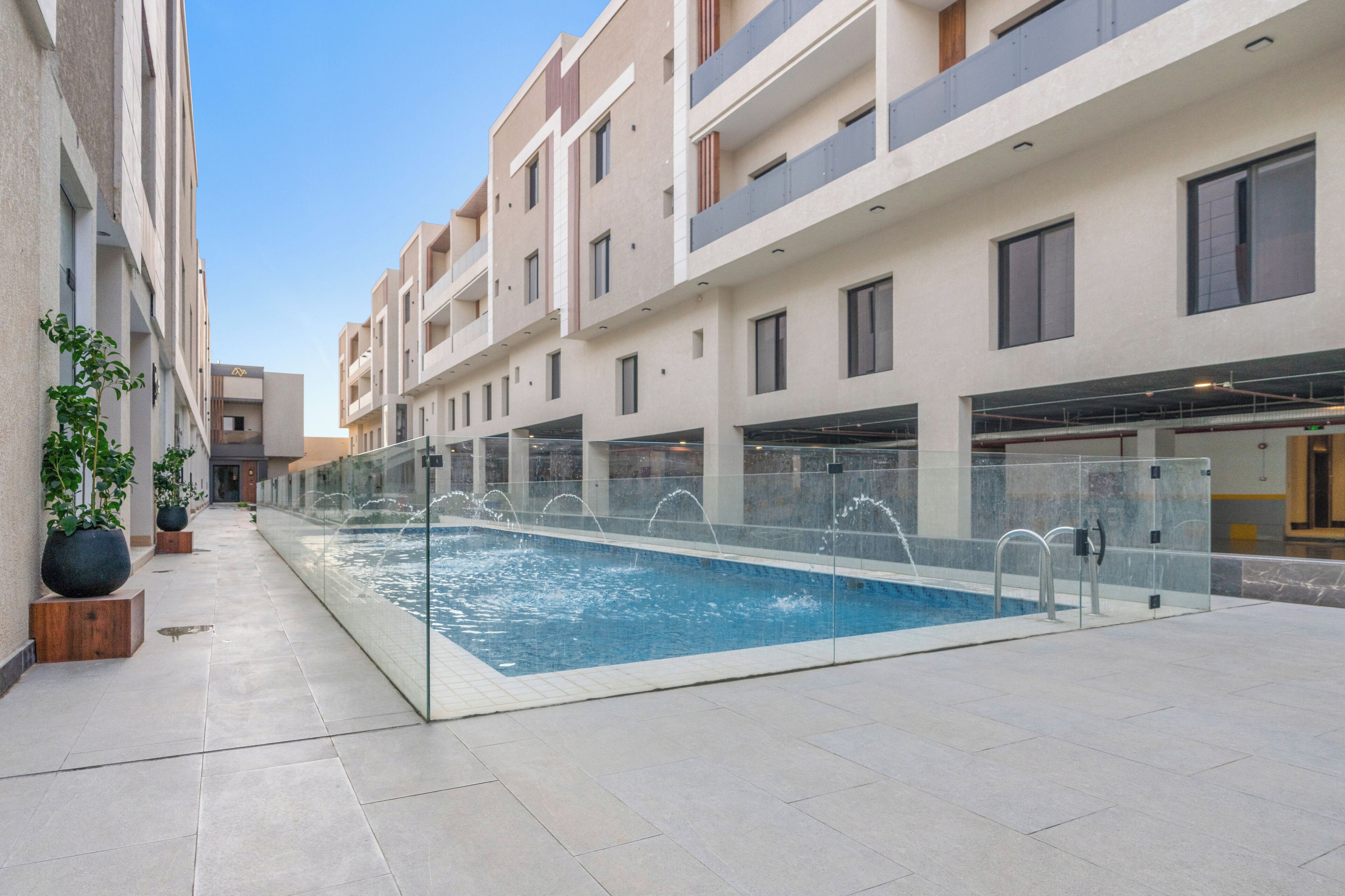 A modern building with a swimming pool, potted plants, and a clear sky.