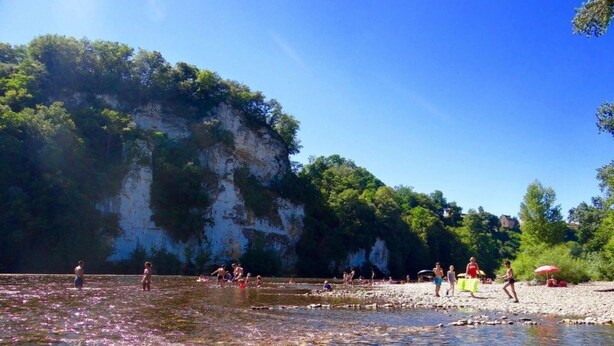 A beach with clear water, people swimming, and a rocky cliff in the background. - Holiday Home in Perigord Noir Near Dordogne (Carsac-Aillac)
