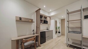 Une cuisine moderne avec un bureau en bois, une chaise et un four à micro-ondes encastré. On y trouve une petite poubelle et une plante en pot près de l’évier.