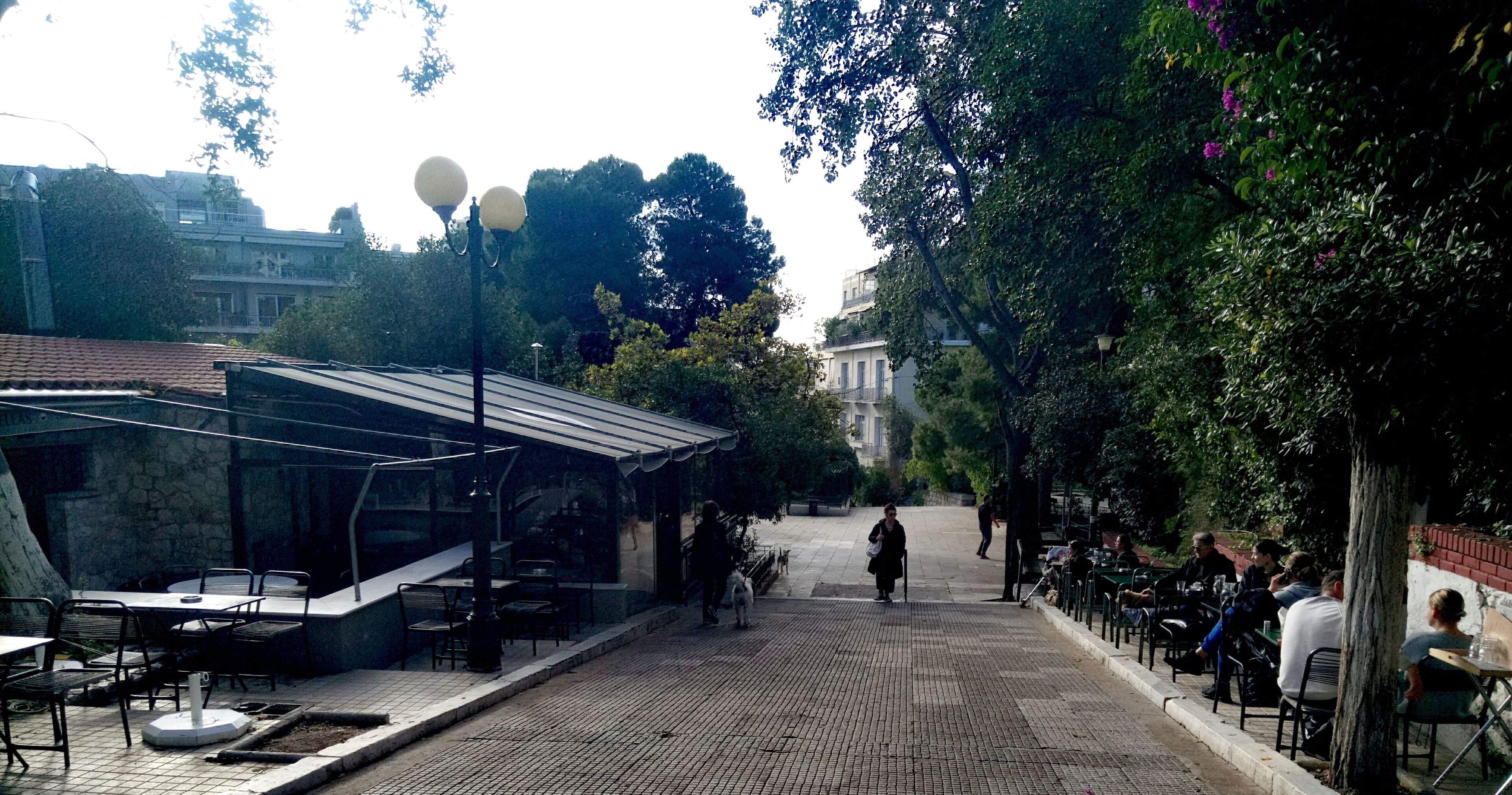 Un caffè all'aperto con tavoli e sedie, una zona con copertura e un viale lastricato.