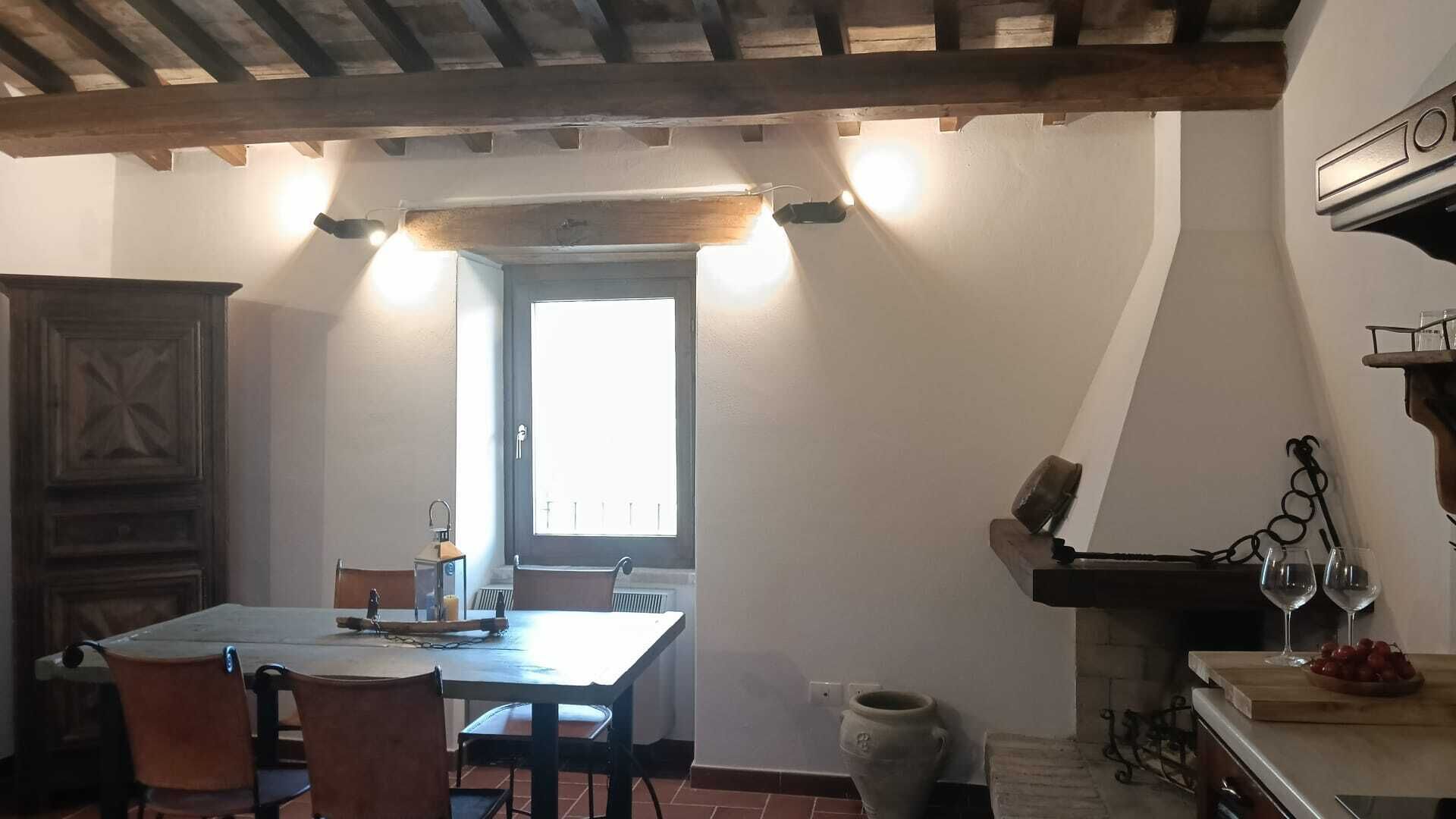 Een eetgedeelte met een houten tafel en stoelen, een kast en een open haard met wijnrek en glazen.