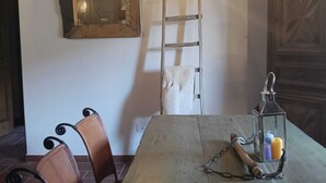 Un comedor rústico con una mesa de madera, dos sillones de cuero, una escalera de madera, un espejo y un farol con velas.
