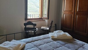 Un dormitorio con cama, dos sillas, un armario de madera y ventana con vistas a un paisaje montañoso.
