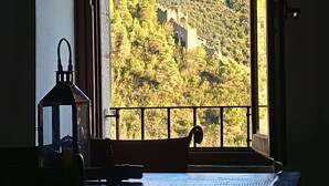 Una habitación con vista a un castillo en una colina, una mesa con camino de mesa y un farol en la pared.