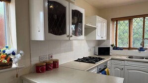 A kitchen with white cabinets, a gas stove, a microwave, and a sink. There are jars on the counter and a window with a view of greenery. - Deluxe Double Room in Birmingham (West Midlands)