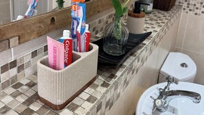 A bathroom with a tiled backsplash, a mirror, a sink, and a toilet. There are toiletries in a holder and a vase with flowers on the counter. - Deluxe Double Room in Birmingham (West Midlands)