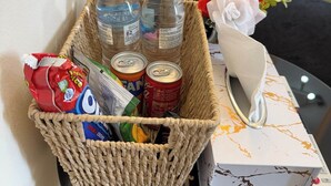 A wicker basket containing bottled water, canned drinks, snacks, and a decorative vase with flowers on a table. - Deluxe Double Room in Birmingham (West Midlands)