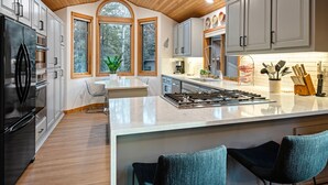 A modern kitchen with a central island, wooden ceiling, and large windows. - Blue Goose in Sunriver Resort (Sunriver)
