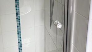 En dusch med ett duschhuvud som kan hållas i handen, en tvålbehållare som också kan hållas i handen och en väggmonterad kontrollpanel.