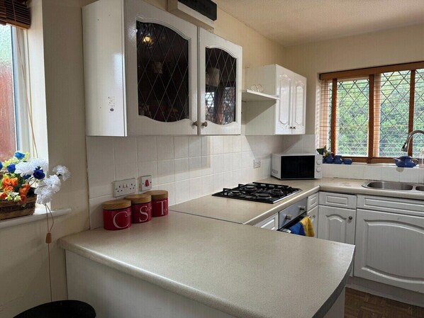 A kitchen with white cabinets, a gas stove, a microwave, and a window with blinds.