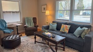 A living room with a brown leather ottoman, a dark grey sofa with patterned cushions, a wooden coffee table, and a patterned rug. - Charming 3-bedroom house with AC and WiFi in Appleton (Appleton)