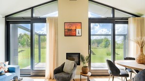 Uma sala de estar moderna com lareira, janelas amplas, área de refeições e vista para o exterior.