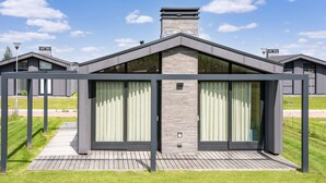 Uma casa moderna com uma grande porta de vidro e janelas, uma chaminé de tijolos e um deck de madeira.