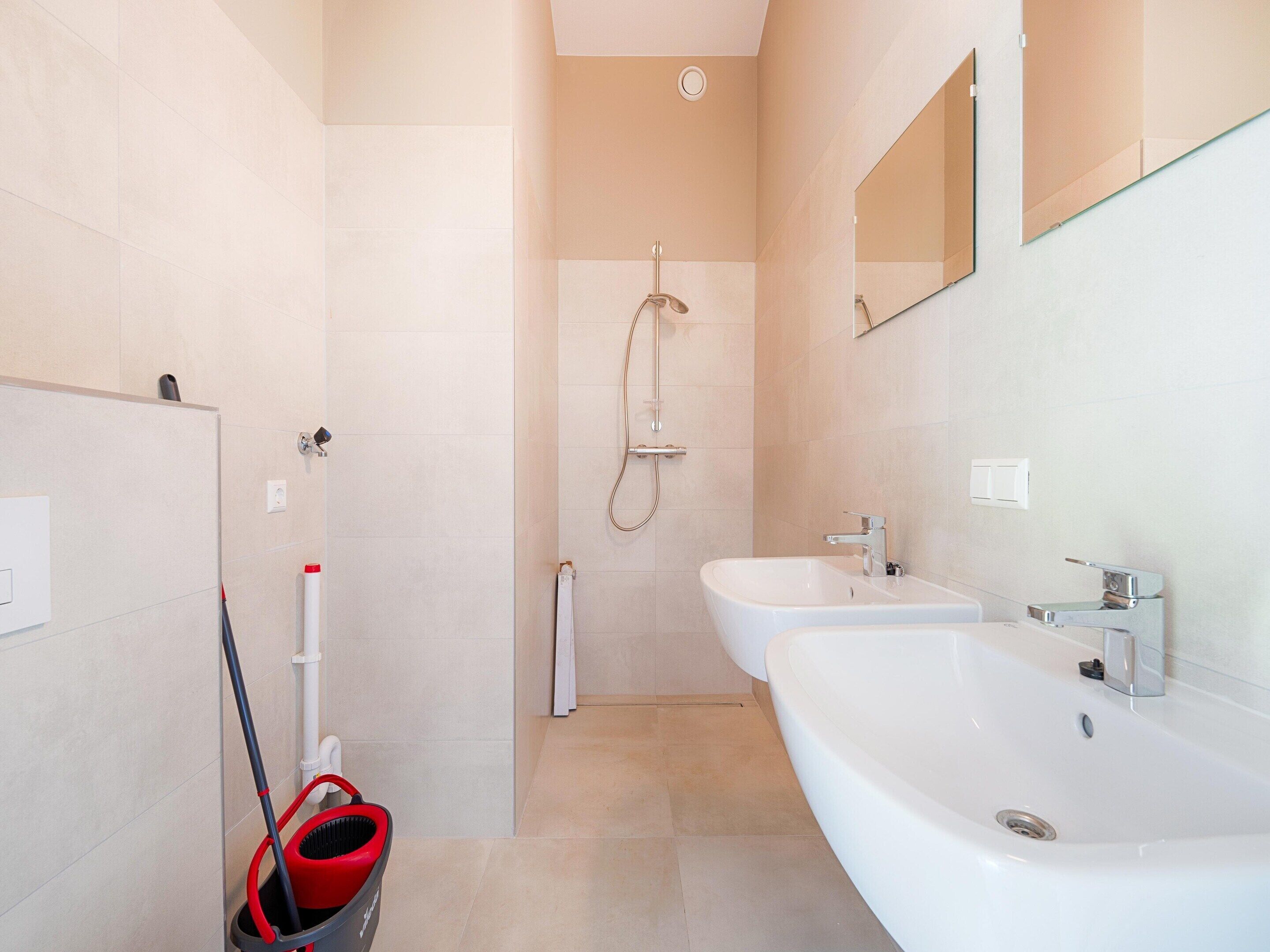 Un baño moderno con dos lavamanos, una ducha y un trapeador.
