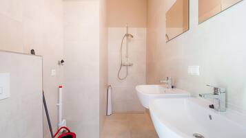 Un baño moderno con dos lavamanos, una ducha y un trapeador.