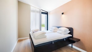 Een moderne slaapkamer met een donker houten bed, wit beddengoed, een klein nachtkastje en een raam met witte gordijnen.