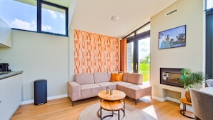 Een moderne woonkamer met een modulaire bank, een ronde houten salontafel en uitzicht op een tuin door grote ramen.