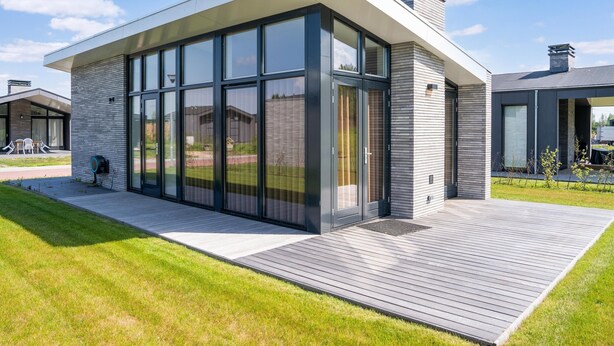 Een modern huis met grote glasramen, een houten terras en een gevel van baksteen.