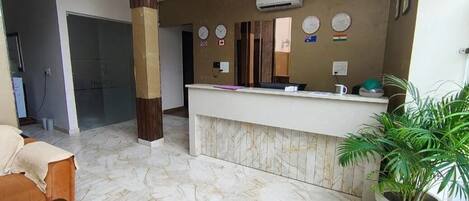 A reception area with a marble floor, a reception desk, a large pillar, and a potted plant.