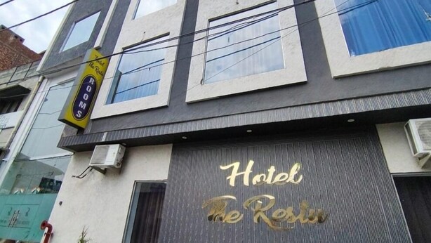 Un hotel con un letrero que dice "Hotel The Resort" y un cartel que indica "Habitaciones" sobre la entrada.