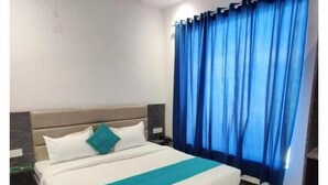 Habitación de hotel con cama, mesita de noche, cortina azul y suelo de madera.