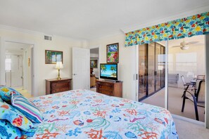A bedroom with a bed, a television, a dresser, and a sliding glass door leading to a balcony.