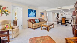 A living room with a sofa, coffee table, and dining area with chairs and a table. - Gulf and Bay Club- C611 by Tropical Sands Accommodations (Siesta Key)