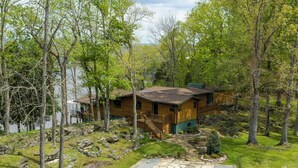 Une cabane en bois avec un chemin de pierre menant à l’entrée, entourée d’arbres et bordée par un plan d’eau.
