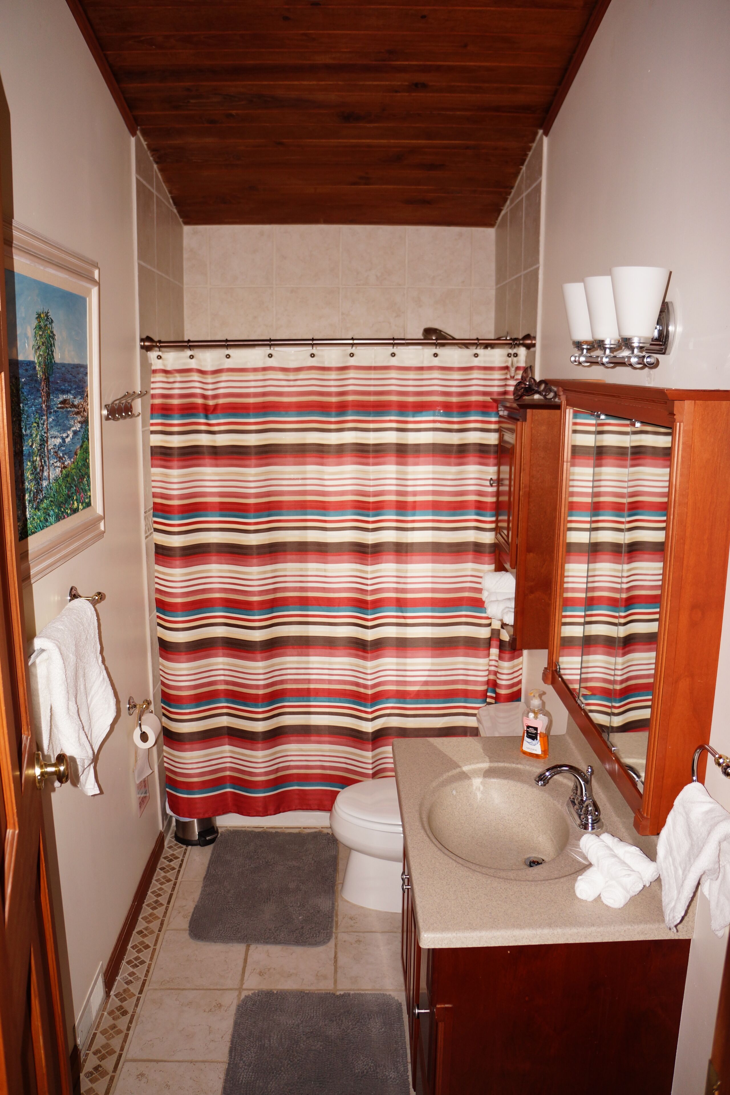 A bathroom with a striped shower curtain, a sink, a mirror, and a toilet.