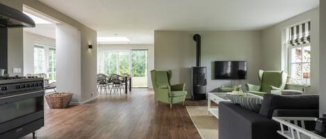 A spacious living room with a fireplace, a dining area with chairs, and a kitchen with a stove.