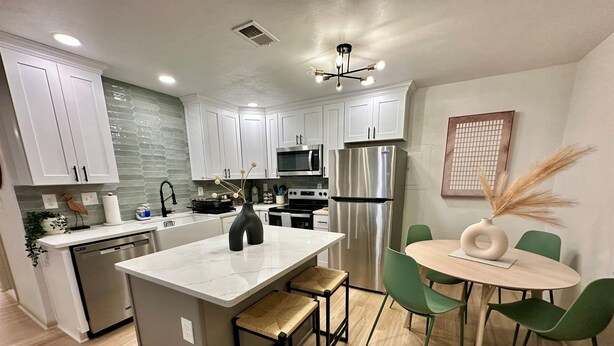 Una cocina moderna con armarios blancos, un refrigerador de acero inoxidable y un comedor con sillas verdes y una mesa redonda.