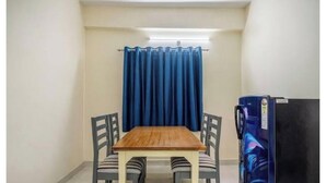 Una habitación pequeña con una mesa de madera, cuatro sillas, una cortina azul y un refrigerador.