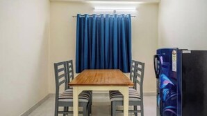 Une petite pièce avec une table en bois et quatre chaises, un rideau bleu et un réfrigérateur.