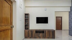 Un salon avec un téléviseur à écran plat fixé au mur, un meuble de rangement en bois et une porte sur le côté gauche.