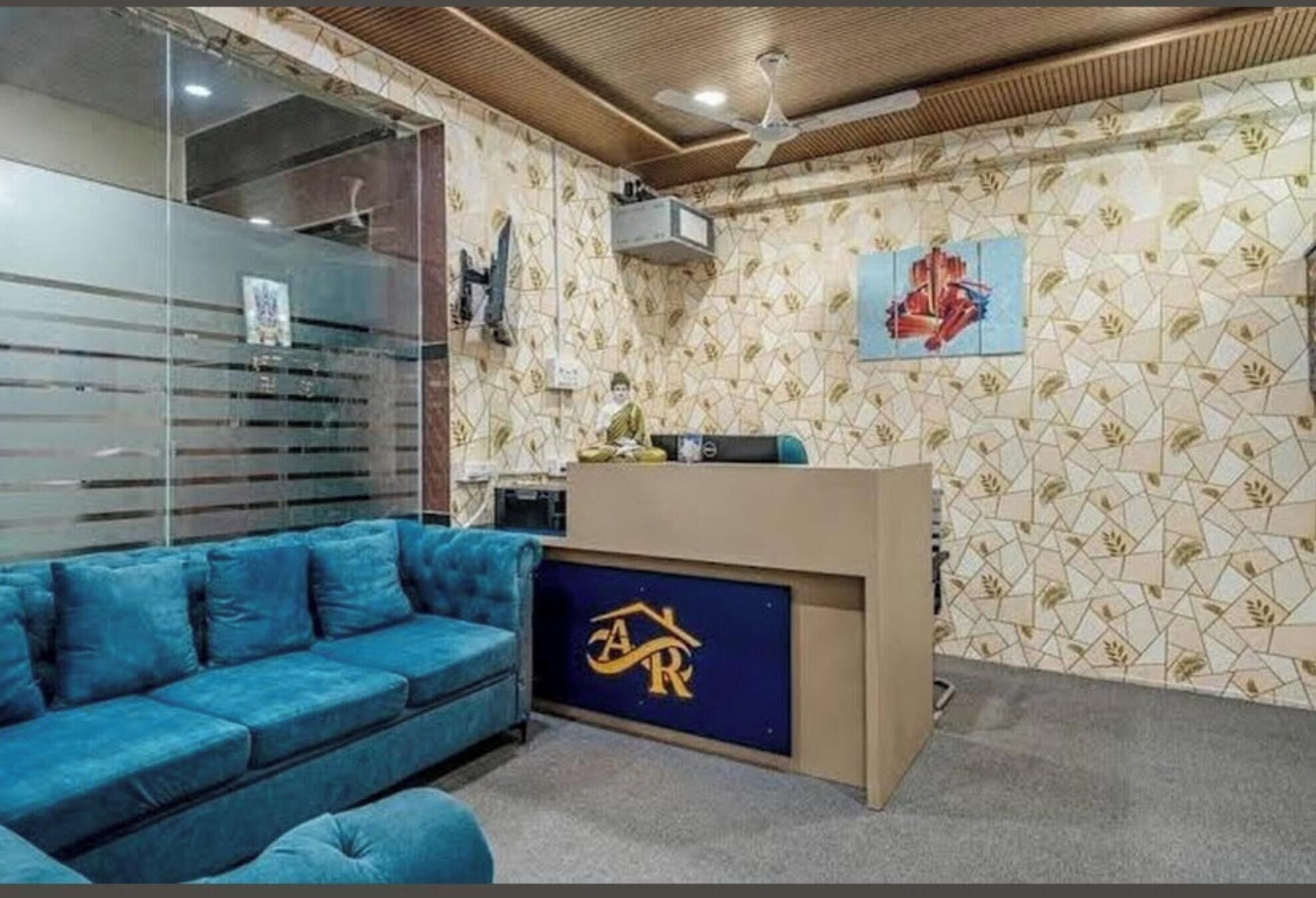 A room with a blue sofa, a wooden ceiling, a patterned wall, and a logo on the desk.