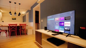 Una sala de estar moderna con un televisor de pantalla plana mostrando la interfaz de un servicio de streaming, una mesa de centro de madera y sillas rojas.